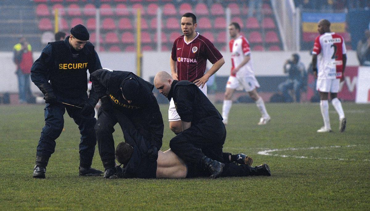 Veiligheidsmensen overmeesteren een fan die het veld opgelopen is tijdens Slavia Praag-Sparta Praag.