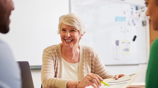 Senior teacher at desk talking to adult education students