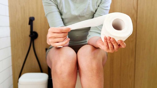 Vrouw met een wc-rol in haar hand zittend op het toilet