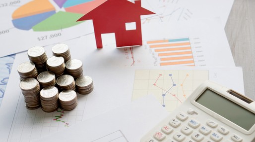 With House Model And Stack Of Coins On Desk