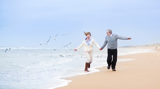 Happy mature couple running at beautiful winter beach with seagulls