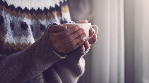 Woman in knitted sweater hands holding cup of warm coffee