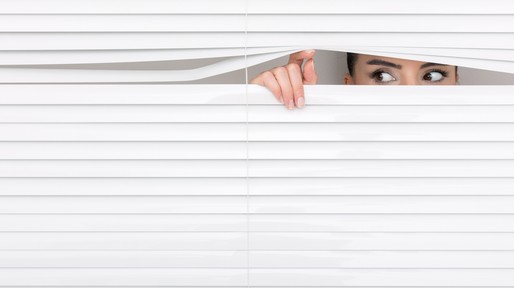 Portrait of a woman looking through out the blinds.